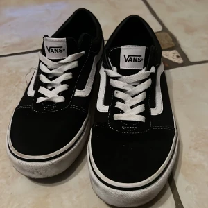 Svarta Vans sneakers - Säljer ett par klassiska svarta Vans sneakers i bra skick. De har vit snörning och den ikoniska vita sidostripen. Perfekta för vardagsbruk och ger en skön streetstyle-look. Sulan är vit med det röda 'Off the Wall'-märket på hälen.