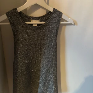 Glittrig ärmlös topp - Snygg glittrig ärmlös topp i silver. Perfekt för festliga tillfällen! Den har en rund halsringning och är i ett stretchigt material som ger en bekväm passform. Passar perfekt till både kjol och byxor för en glamorös look.