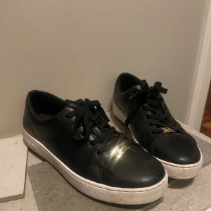 Svarta sneakers med gulddetalj - Säljer ett par svarta sneakers i skinn med snygg gulddetalj på framsidan. De har en vit sula och klassisk snörning. Använd fåtal gånger, Perfekta för både vardag och fest! 🖤✨
