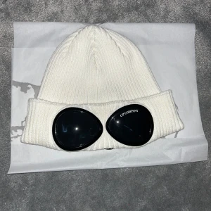 Vit mössa från C.P. Company - Säljer en vit mössa från C.P. Company. Perfekt för att hålla sig varm och stilren under kyliga dagar. Mössan är i storlek M och kommer med originalförpackning. Byten kan diskuteras