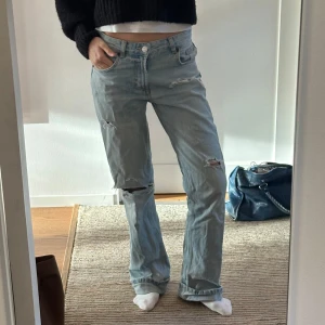 Ljusblå jeans med slitningar - Säljer ett par ljusblå jeans i bra skick med coola slitningar på knäna och låren. Supersnygga till en vit T-shirt! midjemptt 38cm, innerbensmått 87cm