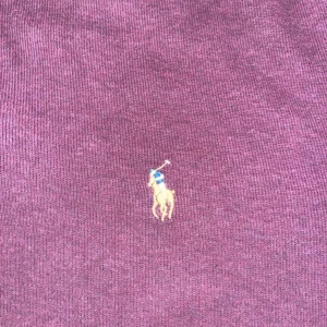 Vinröd tröja från Ralph Lauren - Säljer en snygg vinröd tröja från Ralph Lauren med deras klassiska broderade logga på bröstet. Tröjan är långärmad och perfekt för både höst och vinter. Den är i bra skick och passar perfekt för en stilren look.