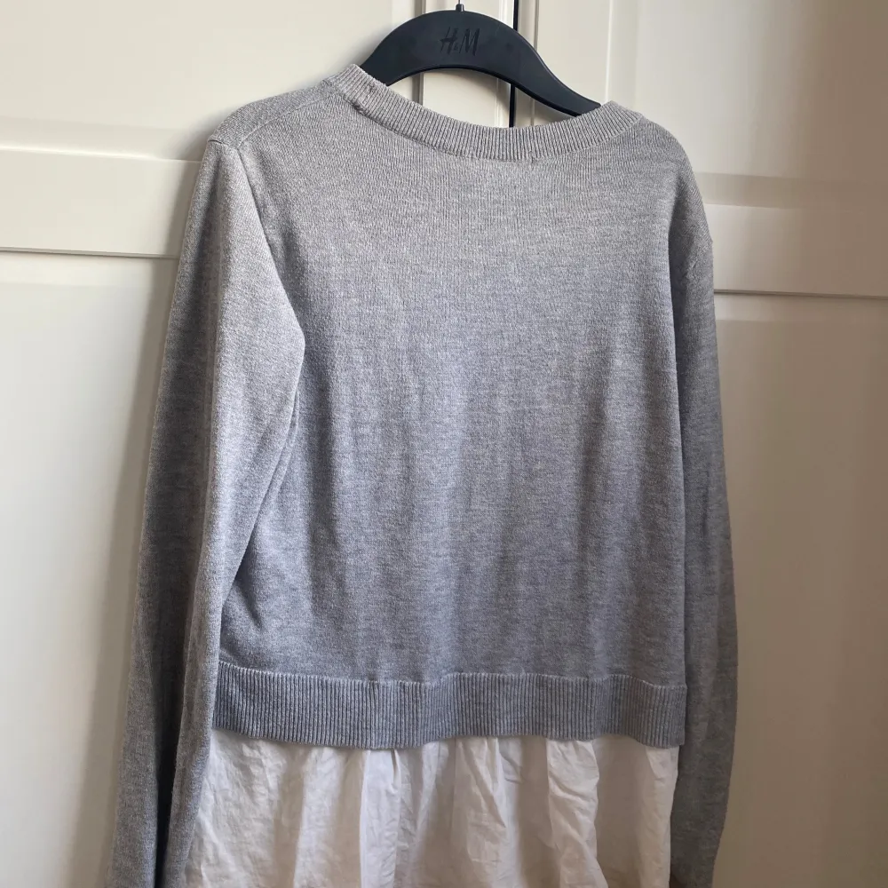 Säljer en snygg grå tröja från H&M med en vit underdel som ger en lager-på-lager-look. Tröjan är långärmad och har en ribbad kant vid ärmslut och nederkant. Perfekt för både vardag och lite finare tillfällen. Superbekväm och stilren! 🌟. Blusar.