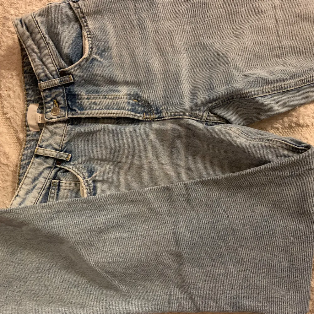 Säljer ett par ljusa jeans i bra skick med coola slitningar på benen. De har en klassisk knappgylf och är perfekta för en avslappnad stil. Passar bra till både vardag och fest! Högmidjade. Jeans & Byxor.