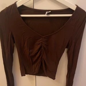Brun långärmad topp - Säljer en snygg brun långärmad topp med rynkdetalj framtill. Toppen har en tight passform och är croppad.
