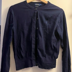 Mörkblå kofta från Ralph Lauren - Säljer en snygg mörkblå kofta från Ralph Lauren. Perfekt för både vardag och lite finare tillfällen. Passar bra till både jeans och kjol! Är i storlek L men passar mer som S/M!
