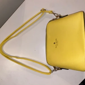 Gul axelväska från Kate Spade - Säljer en superfin gul axelväska från Kate Spade i mycket bra skick. Väskan har en justerbar axelrem och en praktisk dragkedja på baksidan. Perfekt för att lysa upp din outfit! 💛På en av väskans innerfickor har sömmen gått upp som man ser på sista bilden