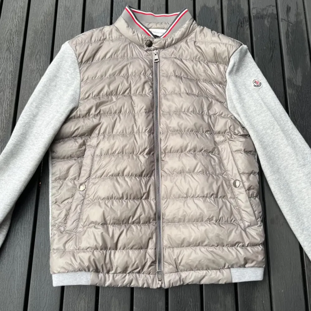 Säljer en snygg grå cardigan från Moncler. Den har en quiltad front med dragkedja och mjuka grå ärmar. Perfekt för höst och vår! Jackan har en stilren design med en liten logga på ärmen. Passar både till vardags och lite finare tillfällen.. Jackor.