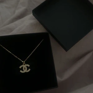 Guldigt halsband med Chanel logga - Säljer ett elegant guldigt halsband med en glittrig logga. Perfekt för att ge en touch av lyx till vilken outfit som helst. Kedjan är fin och smycket är i mycket bra skick. Kommer i en snygg förpackning från Reworked Treasures. Kedjan är 45 cm. Äkthets bevis finns även med! 