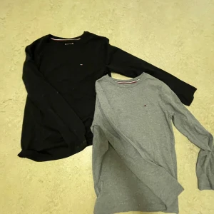 Svart och grå långärmad tröja från Tommy Hilfiger - Två stilrena långärmade tröjor från Tommy Hilfiger i svart och grått. Perfekta för både vardag och lite finare tillfällen. De har en liten logga på bröstet och är gjorda i mjukt bomullsmaterial. Passar bra till jeans eller chinos!