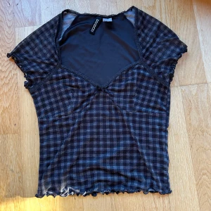 Svart rutig topp från h&m - Svart rutig topp från h&m i ett lätt och luftigt material. Toppen har en v-ringad design med spetsdetaljer och korta ärmar. Perfekt för både vardag och festliga tillfällen. genomskinlig mesh vid magen & armarna 🖤 endast använd 1 gång