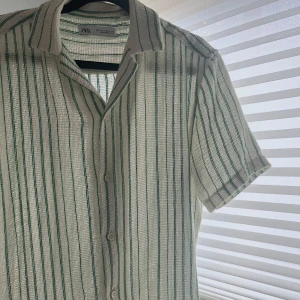 Randig kortärmad skjorta från Zara - Säljer en snygg och luftig skjorta från Zara i grönt och vitt. Skjortan har knappar framtill och är i ett bekvämt material.