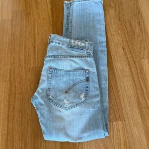 Dondup jeans slim - Säljer ett par ljusblå jeans i bra skick med coola slitningar för en avslappnad look. De har en klassisk femficksdesign och knappgylf. Perfekta för vardagsbruk och ger en trendig touch till din outfit.
