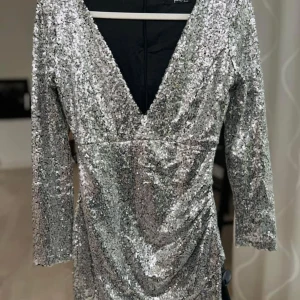 Glittrig silverklänning med v-ringning - Snygg glittrig klänning i silver med v-ringning och trekvartsärmar. Perfekt för festliga tillfällen när du vill glänsa lite extra. Klänningen har en figurnära passform som framhäver dina kurvor. Ett måste för nyårsfesten eller andra speciella tillfällen! ✨