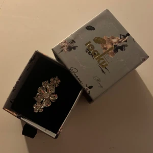 Silverfärgad blomring - Elegant silverfärgad ring med blommotiv. Ringen har detaljerade blommor som ger en stilren och sofistikerad look. Perfekt för att lägga till en touch av elegans till din outfit. Äkta silver, nypris 600kr. Använd ett fåtal gånger, som ny