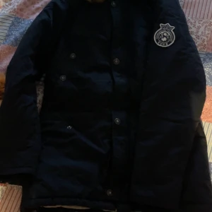 Svart jacka från Svea - Säljer en svart jacka från Svea med tryck på armen Jackan har knappar och är långärmad, perfekt för kyligare dagar. Den är stilren och enkel att matcha med olika outfits.