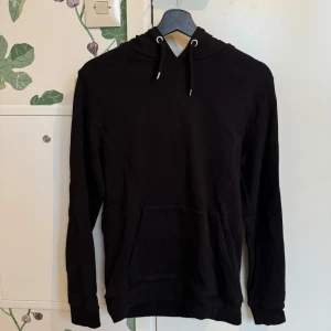 Svart hoodie från ASOS DESIGN - Säljer en stilren svart hoodie från ASOS DESIGN. Den har en klassisk design med huva och dragsko samt en praktisk magficka. Perfekt för en avslappnad look.