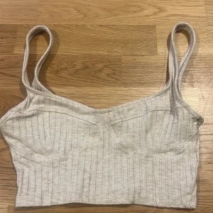 Grå ribbad linnetopp från H&M - Snygg grå ribbad linnetopp från H&M med smala axelband. Perfekt för en avslappnad stil eller som lager under en jacka. Enkel och stilren design som passar till många olika outfits.