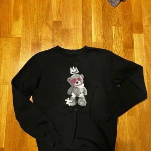 Svart tröja med nallemotiv från Closure London - Säljer en svart tröja från Closure London med ett coolt nallemotiv på framsidan. Tröjan har långa ärmar och en rund halsringning. Perfekt för en avslappnad stil. Tröjan är köpt från Zalando 