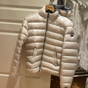 Beige pufferjacka från Colmar - Snygg beige pufferjacka från Colmar med huva och dragkedja. Jackan har en quiltad design och är perfekt för kyligare väder. Den har en stilren look med Colmar-logga på ärmen. Använd 2 gånger men inte mer då den är för liten för mig. NYPRIS: 4500 (pris går att diskuteras)