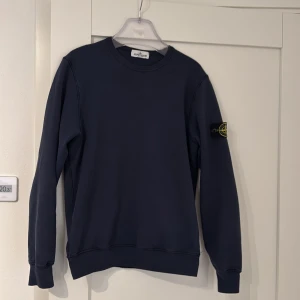 Mörkblå sweatshirt från Stone Island - Säljer en stilren mörkblå sweatshirt från Stone Island. Tröjan har en klassisk rund hals och långa ärmar. Den ikoniska logotypen sitter på ärmen. Perfekt för en avslappnad look.