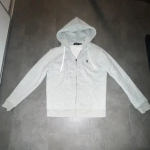 Grå hoodie från Ralph Lauren - Säljer en grå zip up hoodie ifrån Ralph Lauren då den är för stor för mig. Helt oanvänd, storlek L passar M.