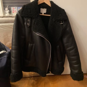 Svart skinnjacka med foder - Snygg svart skinnjacka med mjukt foder och dragkedja. Jackan har en klassisk design med bred krage och spänne vid halsen. Perfekt för kyligare dagar. Storlek xs💕 köptes för 500 säljer för 280💕
