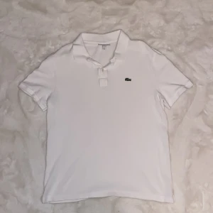 Säljer en jättesnygg kortärmad pikétröja från Lacoste åt min bror🤍 - Säljer en stilren vit pikétröja från Lacoste i slim fit. Säljer åt min bror, pikén är XL men är liten i storlek😊Pikén har korta ärmar och den klassiska krokodilloggan broderad på bröstet. Perfekt våren och jättefin passform👌🏻jätte jätte liten fläck på backsidan av pikén men syns knappt. Annars är den bra skick och den har inga håll eller nått,skriv om funderingar, priset kan diskuteras och lämna gärna omdöme om köpt👍🏻