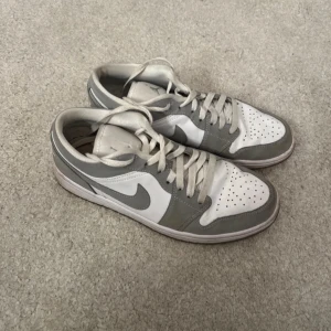 Nike Air Jordan i grått och vitt - Säljer ett par stilrena Nike Air Jordan sneakers i grått och vitt. Skorna har klassisk snörning och den ikoniska Air Jordan-loggan på hälen. Perfekta för en sportig look. De är lite slitna i ena hälen (se bild) men annars i bra skick! Nypris 2000kr🤩