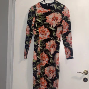 Blommig långärmad klänning - Snygg långärmad klänning med ett blommigt mönster i rosa och grönt på en svart bakgrund. Perfekt för både vardag och speciella tillfällen.