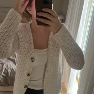 Vit stickad kofta från Zara - Säljer en mysig vit stickad kofta från Zara med knappar framtill. Perfekt för kyliga dagar och ger en stilren look. Koftan har långa ärmar och en bekväm passform.