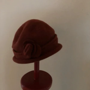 Röd hatt med blomdekoration  - Elegant röd hatt med en dekorativ blomma på sidan. Perfekt för höst och vinter, tillverkad i ull.