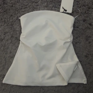 Topp - Topp utan band, lite utsvängd med slits fast med tajt passform! Helt ny med prislapp kvar 