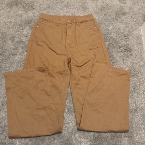 Brun byxor - Säljer ett par stilrena brun byxor med hög midja och rak passform. Perfekta för en avslappnad men ändå snygg look. Byxorna har en klassisk design med knapp och dragkedja framtill.