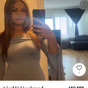 Ljusgrå långklänning - Elegant ljusgrå långklänning med offshoulder-design och långa ärmar. Klänningen har en smickrande slits baktill som ger en stilfull touch.