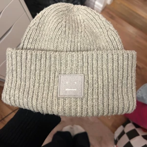 Grå/beige  stickad mössa från Acne Studios - Snygg stickad mössa från Acne Studios med den klassiska loggan fram till. Liiite sminkfläck på insidan men inget som syns när man har på sig den 🥰 fint begagnat skick! Pris går att diskutera vid snabb affär 🫶🏻