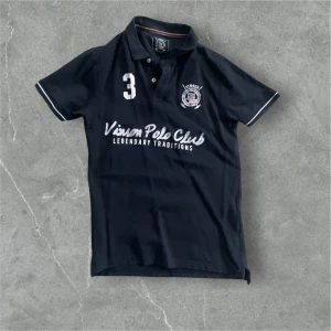 Svart pikétröja chief keef från Vinson Polo Club - Snygg svart pikétröja från Vinson Polo Club med broderad logga och text på bröstet. Tröjan har korta ärmar och en klassisk krage med knappar. Perfekt för en stilren och sportig look. Chief keef polo