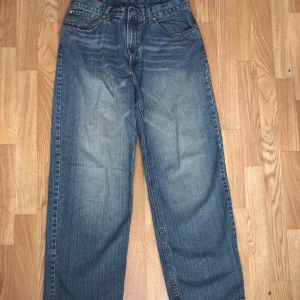 RRJ Baggy/Straight Jeans Unisex  - Säljer ett par klassiska blå jeans från RRI med en avslappnad passform. De har en traditionell femficksdesign och är tillverkade i 100% bomull för en bekväm känsla. Perfekta för en casual look.
