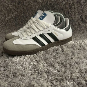 Adidas Samba sneakers - Klassiska Adidas Samba sneakers i vitt och svart med bruna sulor. Skorna är i strl 40,5 men sitter som 40 och dem är i mycket bra skick. 