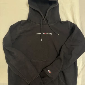 Svart hoodie från Tommy Jeans - Snygg svart hoodie från Tommy Jeans med logga på bröstet. Den har en klassisk känguruficka och justerbar huva med dragsko. Perfekt för en avslappnad stil. Storlek S men lite liten i storleken 🫶🏻