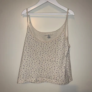 Blommig linnetopp från Brandy Melville - Söt linnetopp från Brandy Melville i beige med små blommor i blått. Perfekt för varma sommardagar eller pyjamas✨✨😄