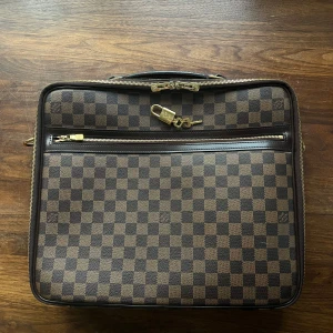 Snygg jobb/skolväska - Snygg väska med klassiskt rutigt mönster i brunt och beige. Väskan har en praktisk dragkedja med hänglås och flera fack för organisering. Perfekt som jobb eller skolväska. Rymmer en dator utan problem :) dustbag ingår. 