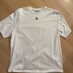 Vit t-shirt från Adidas - Säljer en klassisk vit t-shirt från Adidas med det ikoniska logotypen broderad i svart på bröstet. T-shirten är overzise  och är tillverkad i mjuk bomull. Perfekt för en avslappnad stil. Aldrig använd