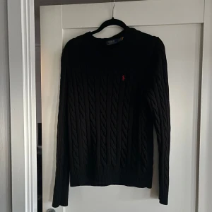 Svart tröja från Ralph Lauren - Säljer en stilren svart kabelstickad tröja från Ralph Lauren. Tröjan har en klassisk design med rund hals och det ikoniska röda logotypbroderiet på bröstet. Perfekt för kyligare dagar. Nästan helt ny använd Max 2 gånger köpt för nån månad sen bara. Köpt för 2400kr på polo butik. Skriv vid frågor svarar snabbt👍🏽