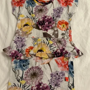 Blommig klänning från Molo - Säljer en färgglad blommig klänning från Molo med volangdetaljer. Klänningen har korta ärmar och ett härligt mönster i olika färger som blå, lila, gul och röd. Perfekt för sommaren! Klänningen kommer tvättas och strykas innan den skickas! ⭐️💞