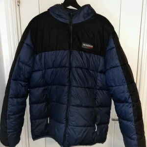Svart och blå pufferjacka från McKenzie - Säljer en svart och blå pufferjacka från McKenzie. Jackan har en dragkedja framtill och en huva för extra skydd. Perfekt för kyliga dagar.