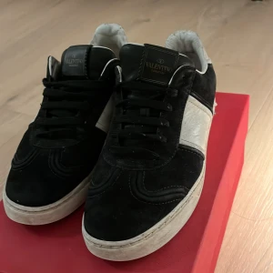 Valentino Garavani sneakers - Snygga Valentino Garavani sneakers i svart och vitt. Skorna har en klassisk design med snörning och en kontrasterande vit panel på sidan. Perfekta för en stilren look. Skorna är väldigt limiterade eftersom dom inte tillverkas längre. Man får även med låda och extra skosnören. Skriv gärna om det är några frågar. Skorna är i storlek 38 men dom är stora i modellen så dom passar även upp till 39-40. Självklart är dom 100% äkta. Helst mötas upp i Stockholm men kan även frakta. Pris kan diskuteras.
