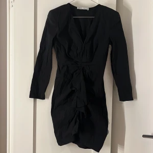 Svart klänning från Zara - Säljer en svart långärmad klänning från Zara. Klänningen har också en volangdetalj framtill och är v ringad i halsen. Använd fåtal gånger