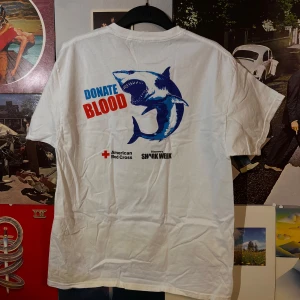 Vit vintage t-shirt från Hanes med hajmotiv - Cool vit t-shirt från Hanes med tryck av en haj och texten 'DONATE BLOOD' och 'DON'T BE COLD-BLOODED'. Perfekt för dig som gillar unika och uppseendeväckande plagg. 🦈