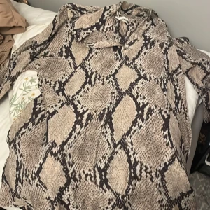 Ormmönstrad klänning från H&M - Säljer en supercool ormmönstrad klänning från H&M. Den har en loose passform och är perfekt för både vardag och fest. Klänningen är i ett mjukt och bekvämt material, vilket gör den skön att bära hela dagen. Ett måste för garderoben om du gillar djurmönster!